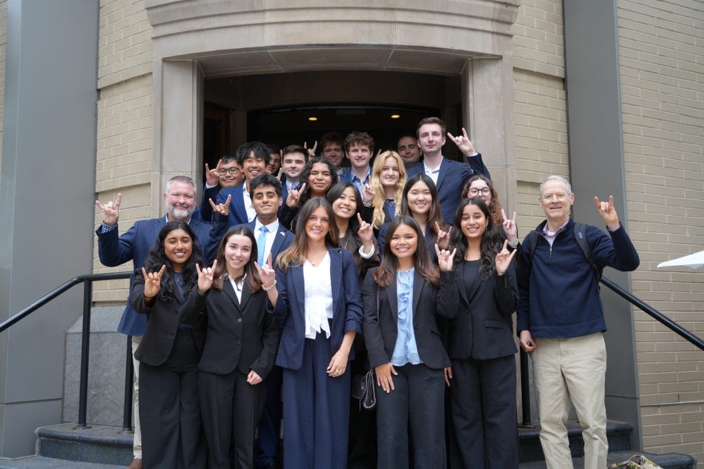 UT Students stand together with hands raised in a hook-em horns symbol